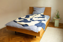 unidorm eichenbett im schlafzimmer parekettboden, blauer Bettwäsche und grünne Sidetable Thoi von bartmann