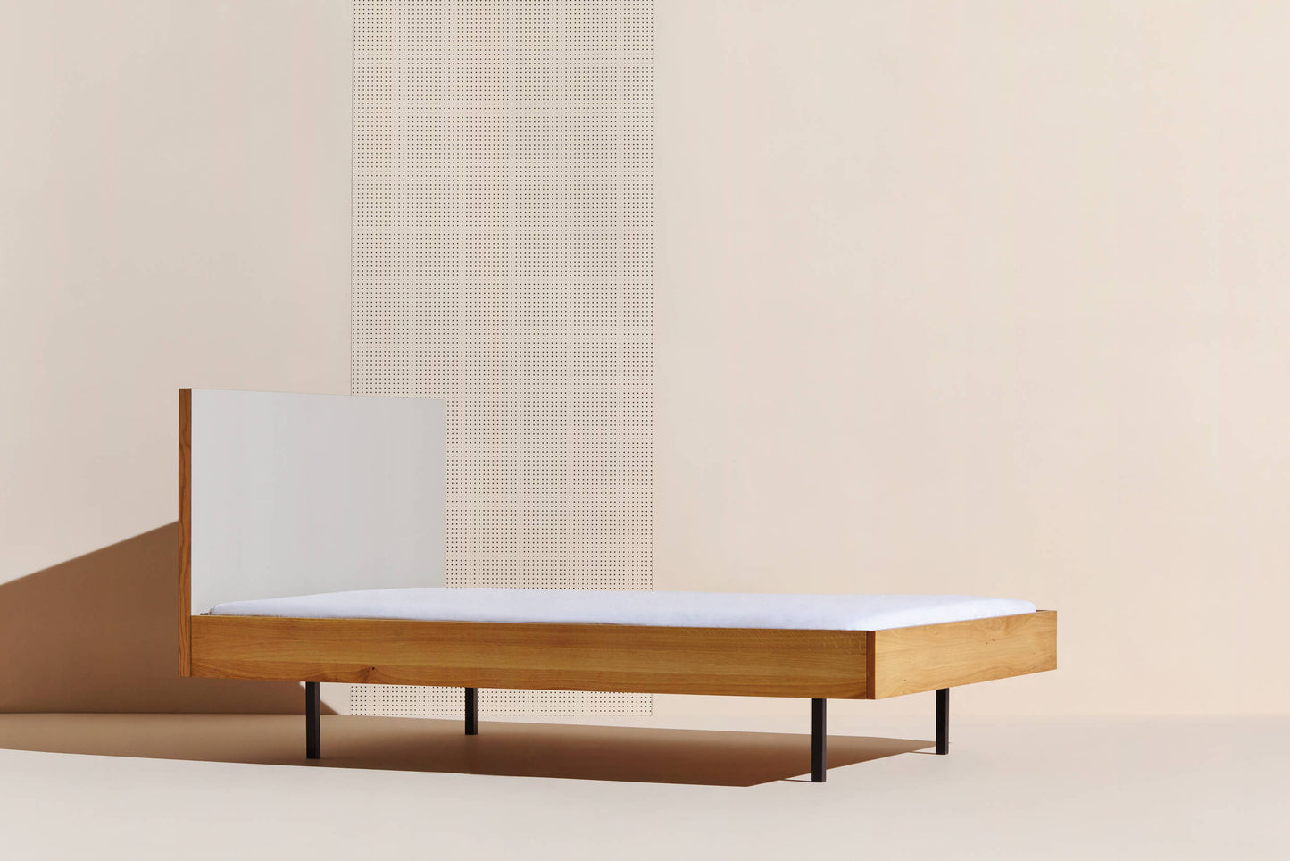 Das Bett Unidorm in Eiche von einer apricotfarbenen Wand mit Schattenwurf