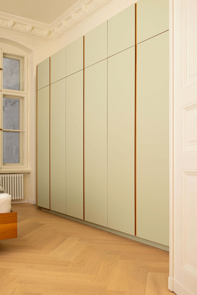 Sicht in einen Raum mit Eichenparkett durch eine Tür. Zusehen ist ein hellgrüner Wandschrank mit Eichegriffleisten