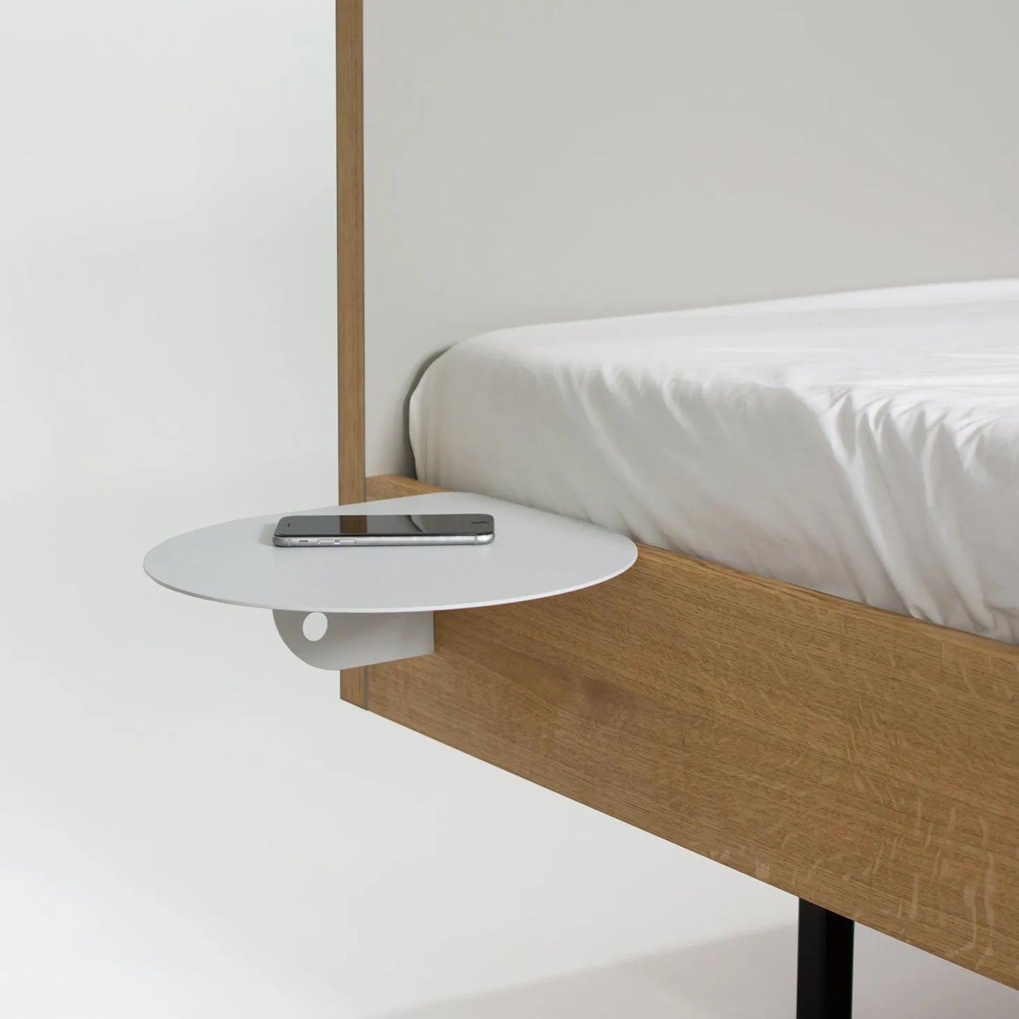 A modern and minimalist bedside table with a curved surface and a laptop or device resting on it, in a simple and clean bedroom setting.