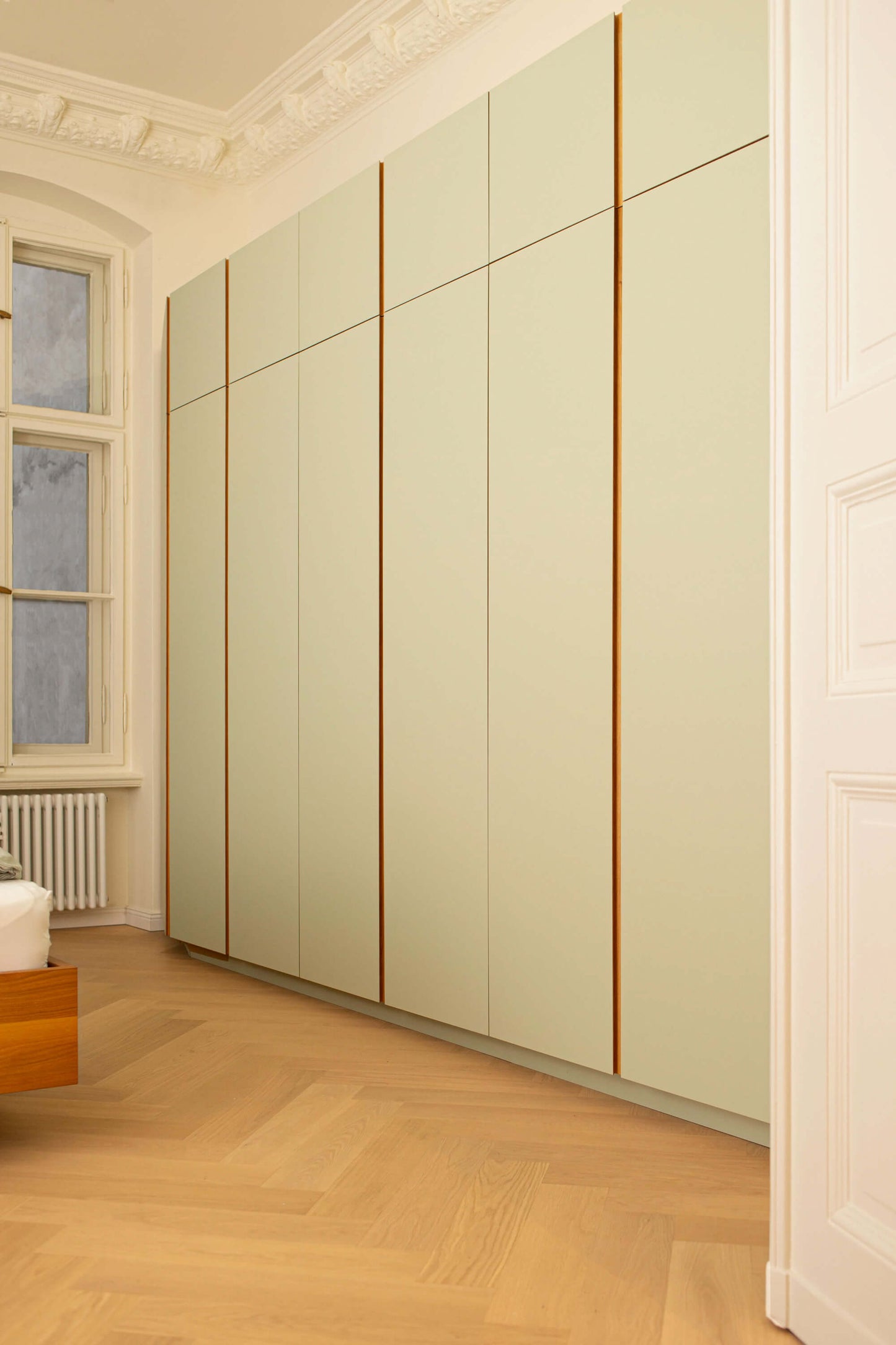 Sicht in einen Raum mit Eichenparkett durch eine Tür. Zusehen ist ein hellgrüner Wandschrank mit Eichegriffleisten